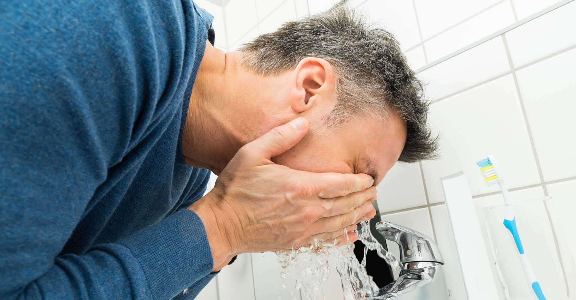 A man washing his face in bathroom sink