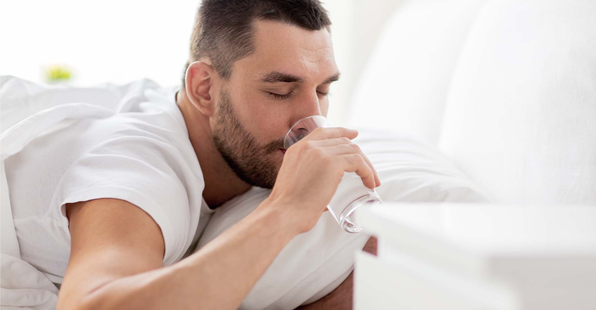 man drinking water in his bed